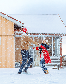 A couple playing in the snow in front of their home