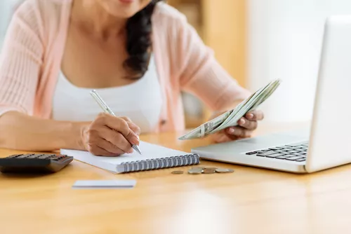 Woman holding money and taking notes in front of a computer