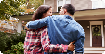 A couple hugs each other in front of their new home.